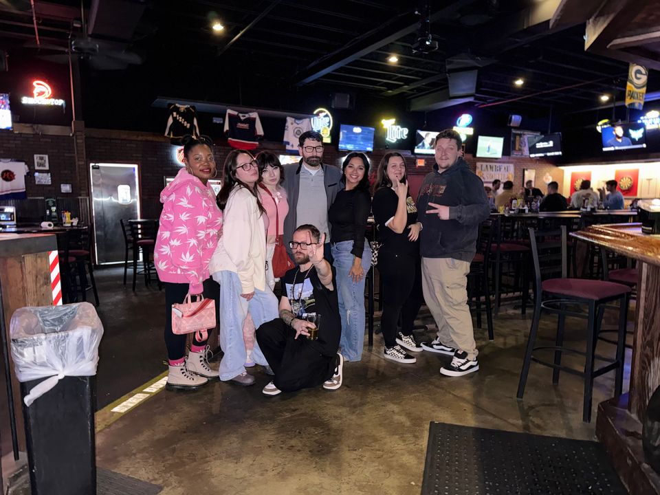 TakTrack kneeling at the front of a big group of friends in a sports bar.