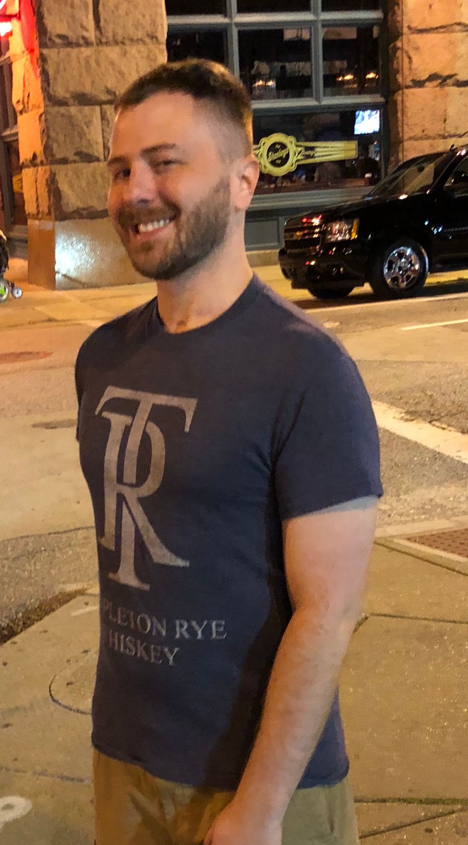 TakTrack smiling on a city sidewalk at night in a gray graphic T-shirt.